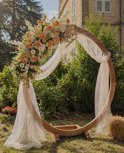 Arche ronde de cérémonie habillée de voilages et de bouquets champêtres