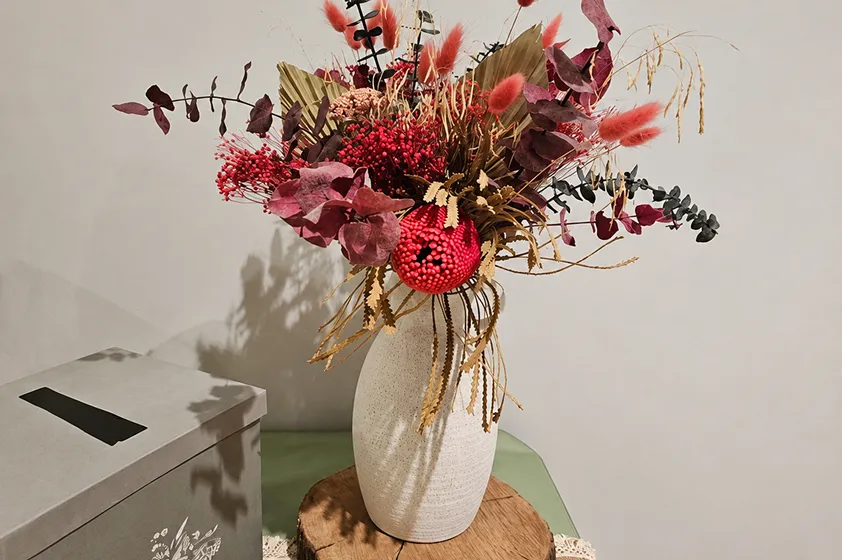 Bouquet rose et vert dans un vase blanc, posé sur un tronc