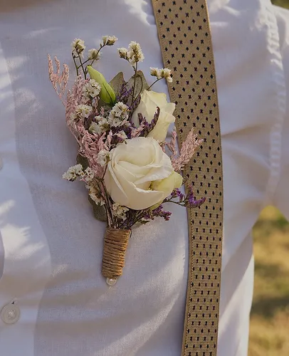 Boutonnière de rose blanche et de fleurs séchées sur la veste du marié