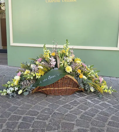 Composition florale de deuil en panier d’osier devant la boutique
