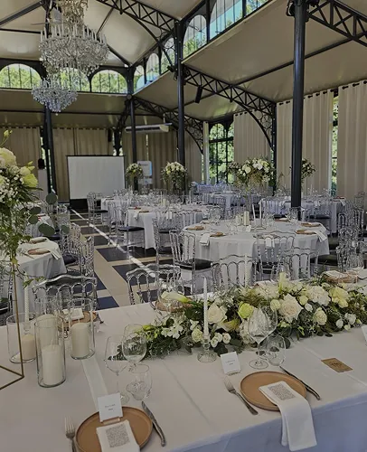 Salle de réception dressée de longues tables fleuries sous une verrière
