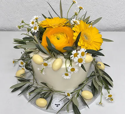 Gâteau de fête couronné de gerberas jaunes, de marguerites et de feuillage